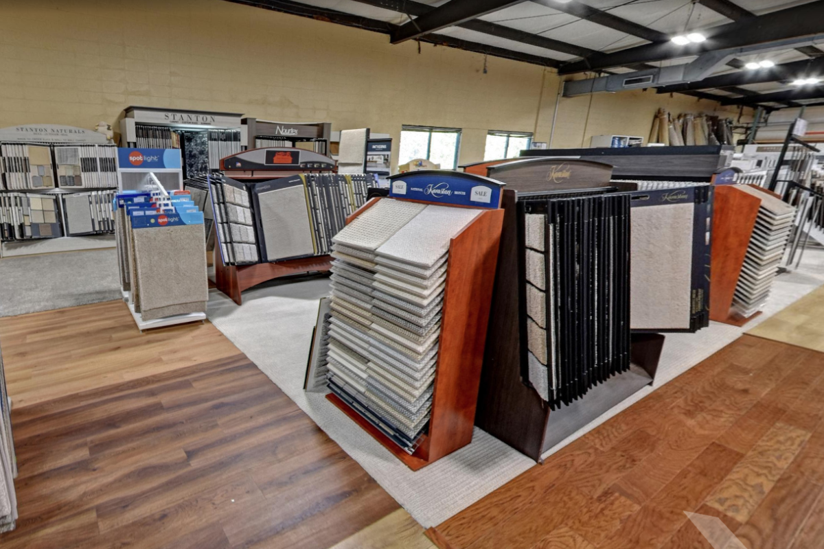 Tim Hogan's showroom displaying various carpet and flooring samples on display racks. The flooring includes wood-look planks and carpet tiles in various colors and textures.